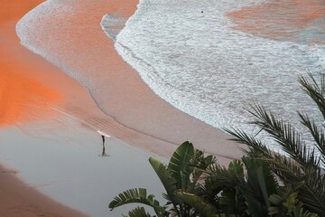 Surfer carrying a surfboard at sunset in Magic Bay, Imsouane, Morocco