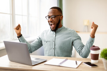 Business Success. African American Businessman At Laptop Shaking Fists And Shouting In Joy Celebrating Career Promotion Sitting At Workplace In Modern Office. Successful Entrepreneurship Concept