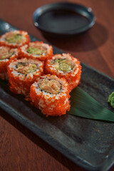 Delicious Close-Up of Sushi Rolls Topped with Vibrant Orange Fish Eggs and Accompanied by Soy Sauce and Wasabi on a Stylish Plate