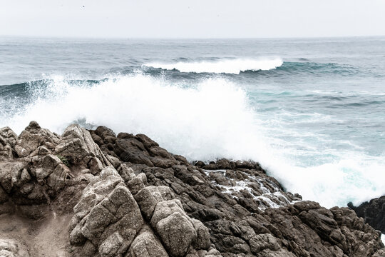 Wave Crashes Along Rocky Cliff in Pebble Beach, CA Foggy Day - Powered by Adobe