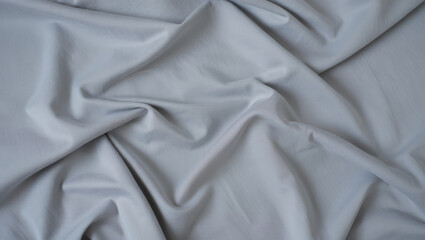 Obraz premium Top-down view of a soft light grey fabric with drapes and folds, creating a simple abstract background. 
