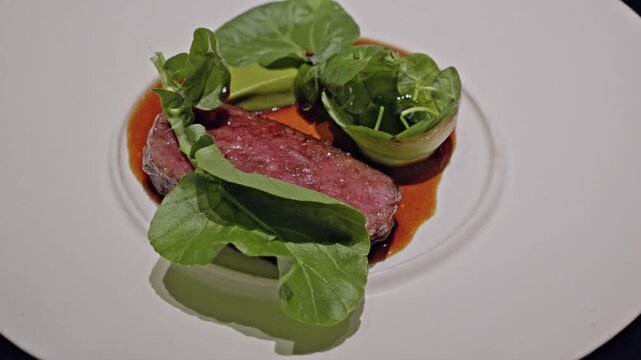 seared slice of Blackmore Wagyu beef is served with leafy greens and a rich jus on a white ceramic plate. highlight the marbling and tenderness of the beef, elegantly plated in a fine dining setting.