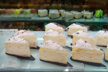 Delicious layered cake slices with whipped cream and rose petals displayed in a pastry shop