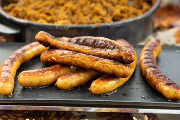 Grilled sausages arranged on a black platter with a background of cooked meat dish