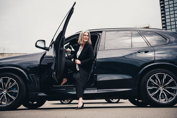 Successful mature businesswoman stepping out of an elegant car in an urban setting on a daytime...