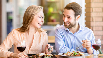 Lovely lady with her boyfriend eating salad and drinking wine, celebrating anniversary together at...