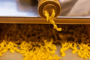 Freshly extruded pasta shapes cascading from a pasta machine onto a wooden surface