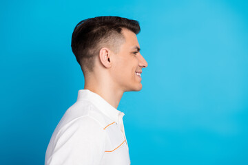 Side profile of a smiling man in a white shirt against a bright blue background expressing...