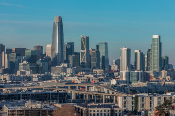 Daytime panoramic view of San Francisco skyline under clear blue sky, highlighting downtown skyscrapers and city layout.