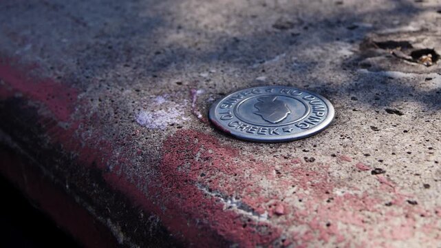 Storm drain with a &ldquo;No Dumping &ndash; Drains to Creek&rdquo; marker placed on a city curb with fish symbol, promoting environmental awareness