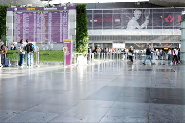 Fototapeta premium People waiting at an airport terminal near a flight information display board and a large advertisement.