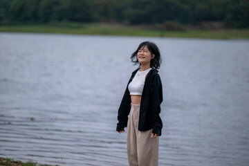 A woman stands on a beach near a body of water, wearing a black jacket