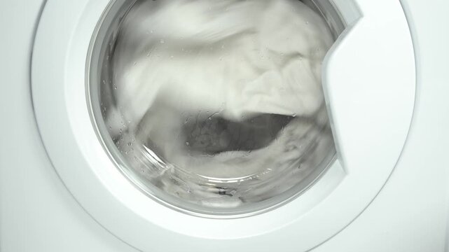 Washing machine washes white clothing and sheets. Cylinder spinning. Nobody