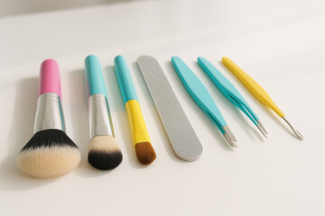 Colorful makeup brushes, nail file, and tweezers arranged neatly on white table for beauty routine and grooming essentials