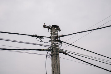 A weathered wooden utility pole with multiple electrical wires against a cloudy sky.  Industrial,...