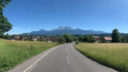Fototapeta premium Rural road leads to a mountain range backdrop, with fields on both sides under blue skies