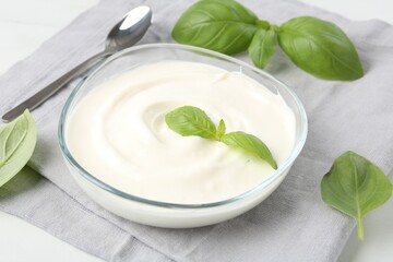 Tasty yoghurt with basil in bowl on white table, closeup