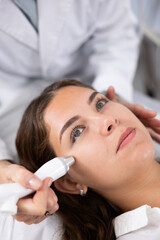 Pleased young woman having face laser therapy by means of apparatus for aesthetic procedures