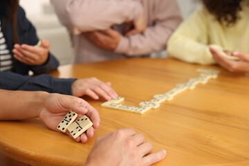 Friends playing dominoes at wooden table, closeup