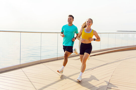 Joyful couple jogging along a serene waterfront pathway embraced by refreshing ocean air - Powered by Adobe