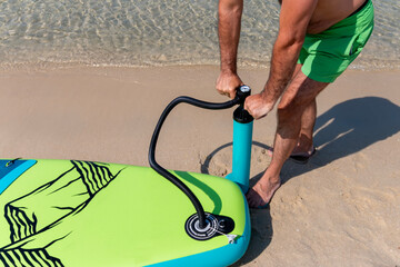 A mature man inflating his paddle board on the beach with a sea background. A senior male getting...