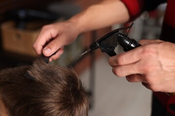 Professional barber working with little boy in barbershop, closeup