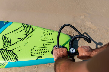 A mature man inflating his paddle board on the beach with a sea background. A senior male getting...