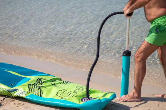 A mature man inflating his paddle board on the beach with a sea background. A senior male getting ready for some fun on a sunny day. Close up.