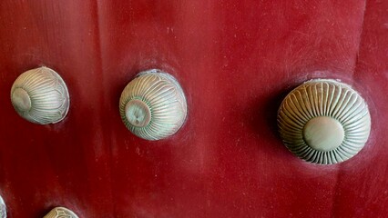 Singapore, Buddha Tooth Relic Temple - 5 July 2025. Radial-patterned bronze studs decorate a red temple door with visible age and surface wear.