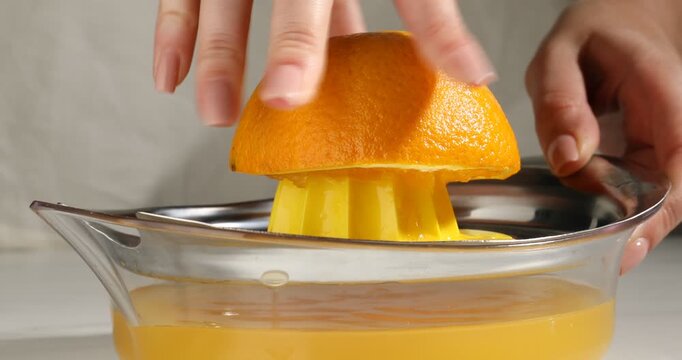 Making juice. Woman with orange using juicer at table, closeup