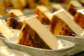 
San Sebastian cheesecake and tiramisu desserts on white plates in a pastry shop display case....