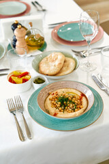 A beautifully arranged table featuring a delicious plate of hummus topped with chickpeas, fresh herbs, pita bread, and a variety of colorful accompaniments in elegant dishware.