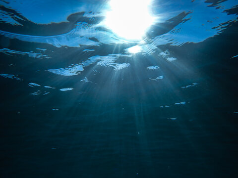 Dark blue ocean surface seen from underwater. Abstract waves underwater and rays of sunlight shining through, Sun light rays undersea deep, Underwater background with sea bottom, Mediterranean sea.