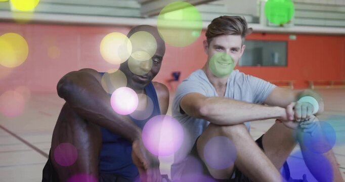 Two fitness partners hearing coach remarks and shifting stance on gym floor, bokeh circles drifting