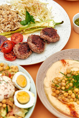 A Deliciously Plated Meal Featuring Savory Meat Patties, Fresh Vegetables, Creamy Hummus, and Fluffy Rice on a Vibrant Table Setting