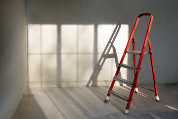 Red ladder stepladder in empty room, without renovation. grey background. Repair concept. © Irina