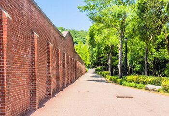 A long brick wall lines a tree-shaded pathway in a serene outdoor setting in Seoul, South Korea