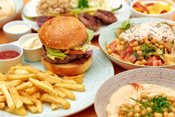 A Delicious Spread of Burgers, Fries, Hummus, and Fresh Salads Showcasing a Variety of Flavorful Gastronomic Delights on a Wooden Table