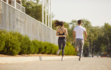 Back view of sporty couple man and woman wearing sportswear jogging together in the park. People...