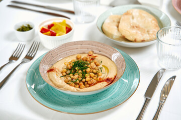 Delicious Plate of Hummus Topped with Chickpeas and Garnished with Herbs Served Alongside Fresh Bread and Accompaniments