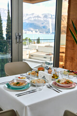 A Lavish Breakfast Table with Diverse Dishes Set Against a Scenic Vista of Mountains and Water in a...