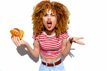 Angry woman with curly hair holding a burger in a striped shirt, expressing frustration Food choice, emotion, and trendy style captured in vibrant colors