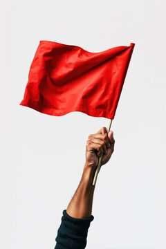 Hand holding up a bright red flag on pole against plain white background symbolizing warning danger alert or protest concept