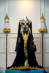A luxurious traditional black wedding gown with golden embroidery and batik motifs, displayed...