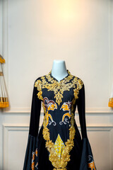 Close-up of a luxurious black wedding gown featuring golden embroidery and batik wayang motifs,...