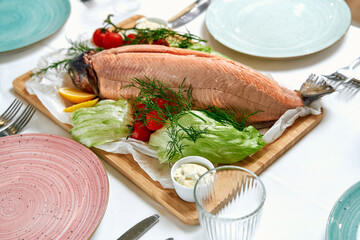 A beautifully presented whole salmon garnished with fresh herbs and surrounded by vibrant...