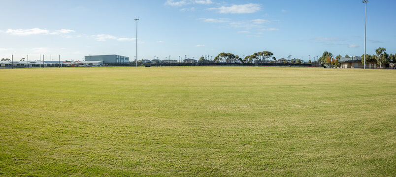 Panoramic view of a well-maintained sports ground in Tarneit, suburban Melbourne, Australia. Large grassy field surrounded by fencing, light poles, and utility buildings, for community activities.