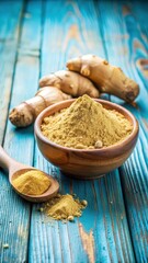 Ginger powder in a shallow bowl sits atop a slice of fresh ginger root on a blue wooden background