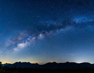 Naklejka premium Panoramic night sky with Milky Way galaxy over mountain silhouettes, filled with stars in a clear atmosphere
