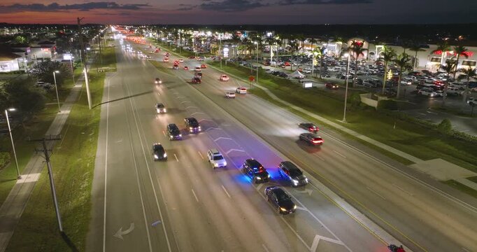 Police vehicle with emergency lights stops a driver for speeding on city road at night in the United States. Traffic moving rapidly on wide highway street.